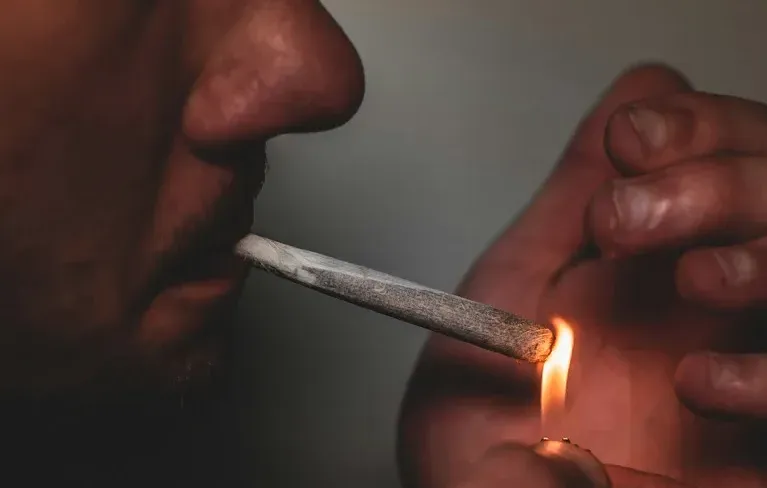  Ein Mann im Profil entzündet sich einen Joint und hält die andere Hand schützend um die Flamme.